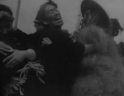 A happy Japanese couple in peasant dress, seen in medium shot, laugh and embrace as a crowd celebrates around them