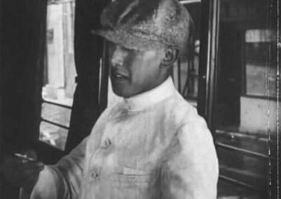 A young Japanese man sitting in a bus in modern (1920s) dress, his face partly obscured by a hat