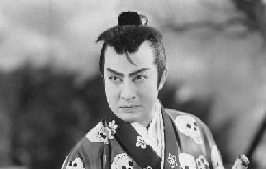 A Japanese man in feudal costume, probably in early middle age, looks to one side of the picture frame against a background of trees